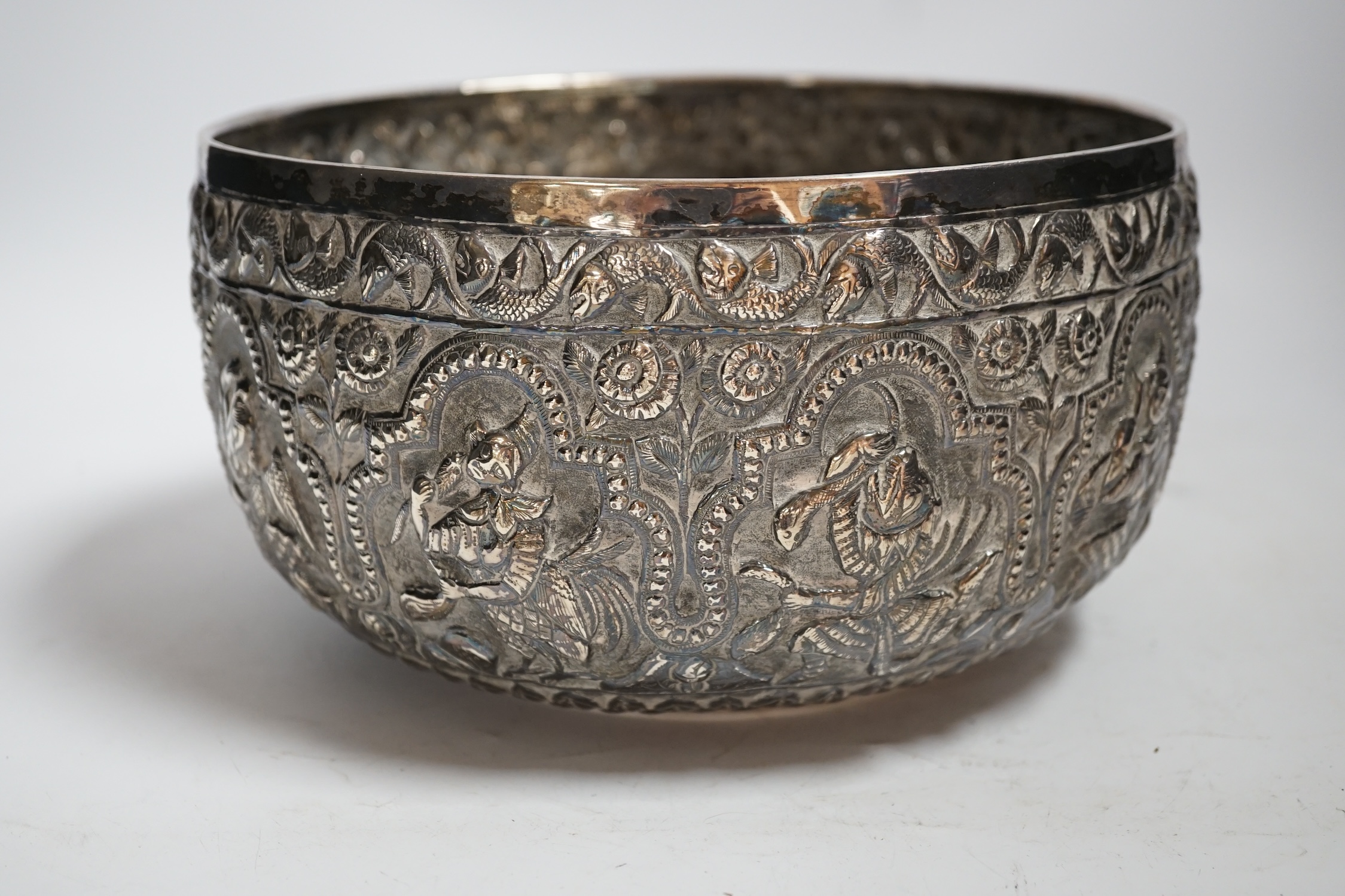 A 19th century Burmese embossed white metal bowl, decorated with figures and flowers, diameter 22.2cm, 22.9oz.